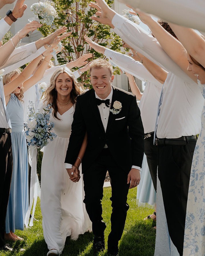 Josh and Shelbi Sanders walking hand in hand under an arch of friends' raised arms on their wedding day